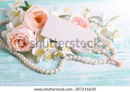 Sweet pastel roses and jasmine flowers and empty tag in ray of light  on turquoise wooden background. Place for text. Selective focus.