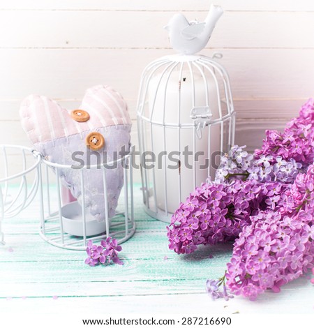 Background  with fresh lilac flowers, candle in decorative bird cage and decorative  heart   on turquoise painted wooden planks against white wall. Selective focus. Square image.