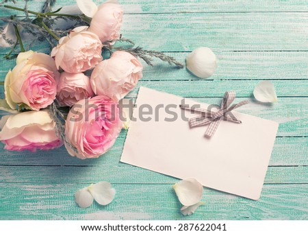 Postcard with fresh roses flowers and empty tag for your text on turquoise painted wooden background. Selective focus. Toned image.