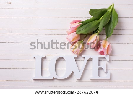 Fresh  spring  pink  tulips and word love  on white  painted wooden background. Selective focus. Place for text.