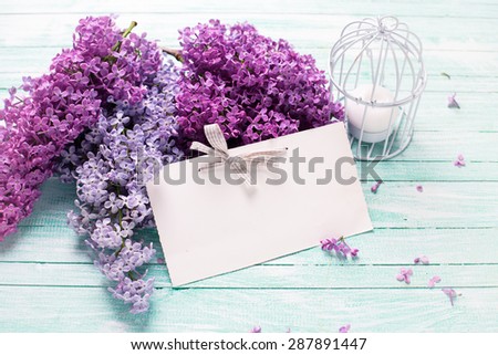 Background  with fresh lilac flowers,  candle and empty tag on turquoise painted wooden planks. Selective focus. Place for text. Toned image.