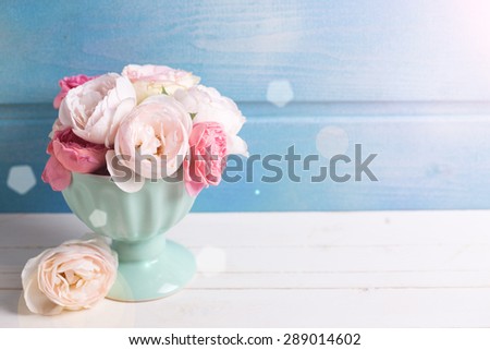Pastel roses in turquoise vase in ray of light on white wooden  background against blue wall. Place for text. Selective focus.