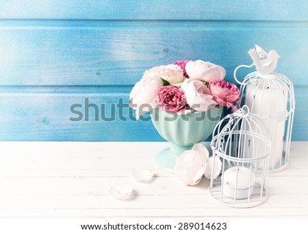 Pastel roses in turquoise vase and candles on white wooden  background against blue wall. Place for text. Selective focus. Toned image.