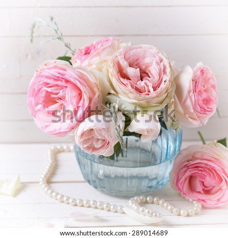 Background with sweet pink roses flowers  in blue vase on white painted wooden background. Selective focus. Place for text. Square image.