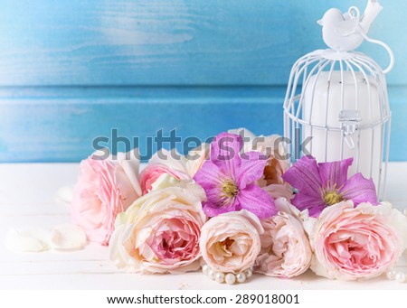 Pastel pink roses, clematis flowers and candle on white wooden background against blue wall. Place for text. Selective focus. Toned image.