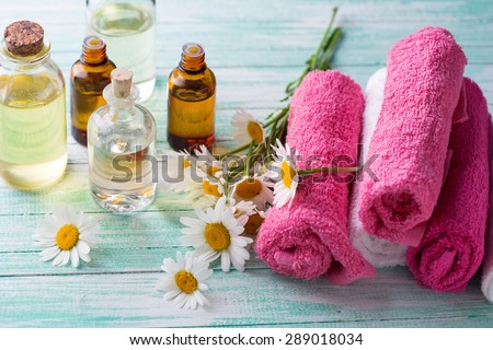 Bottles with essential aroma oil with chamomile and towels on  turquoise painted wooden background. Spa setting. Selective focus.