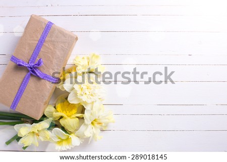 Spring flowers narcissus and box with present  in ray of light on white painted wooden planks. Selective focus. Place for text.