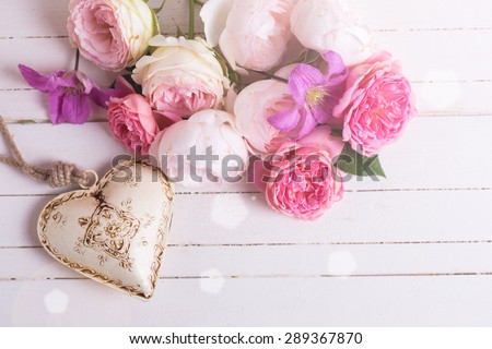 Sweet pastel roses, clematis flowers and decorative heart in ray of light on white  wooden background. Place for text. Selective focus.