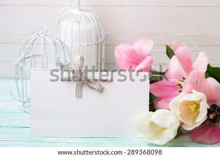 Background with fresh tulips and empty tag for your text on turquoise painted planks against white wall. Selective focus.