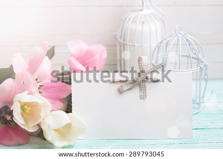 Background with fresh tulips and empty tag for your text  in ray of light on turquoise painted planks against white wall. Selective focus.