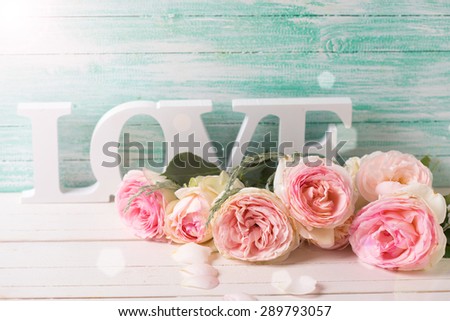 Postcard with sweet pink roses flowers and word love  in ray of light on white painted wooden background against turquoise wall. Selective focus. Place for text.