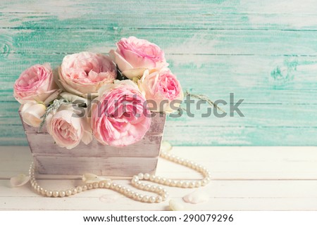 Background with sweet pink roses flowers wooden box on white painted wooden background against turquoise wall. Selective focus. Place for text. Toned image.