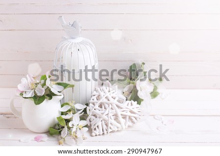 Background  with tender apple blossom, decorative heart and candle in decorative bird cage in ray of light  on white painted wooden planks. Selective focus.