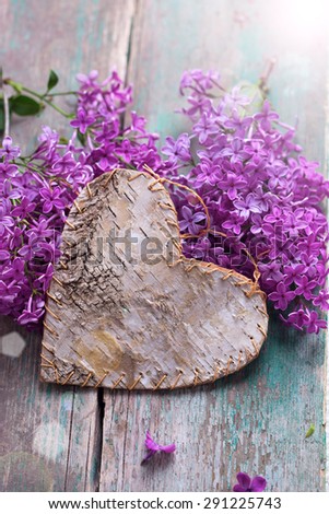 Postcard with  decorative heart and fresh lilac flowers in ray of light  on green aged wooden background. Selective focus.