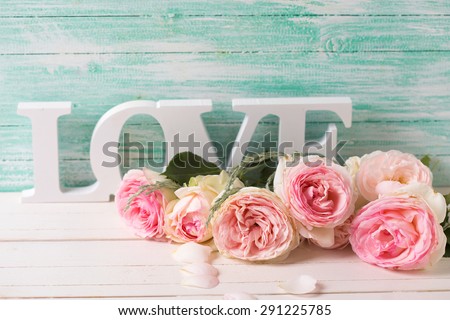 Postcard with sweet pink roses flowers and word love on white painted wooden background against turquoise wall. Selective focus. Place for text.