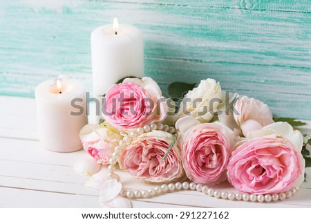 Background with sweet pink roses flowers and candles  on white painted wooden background against turquoise wall. Selective focus.