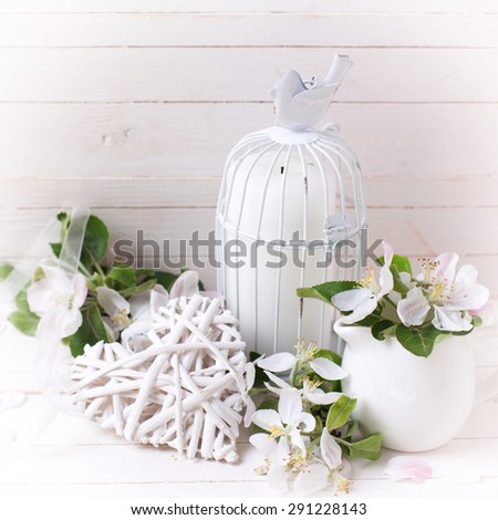 Background  with  decorative heart, tender apple blossom, candles in decorative bird cages in ray of light   on white painted wooden planks. Selective focus is on heart.