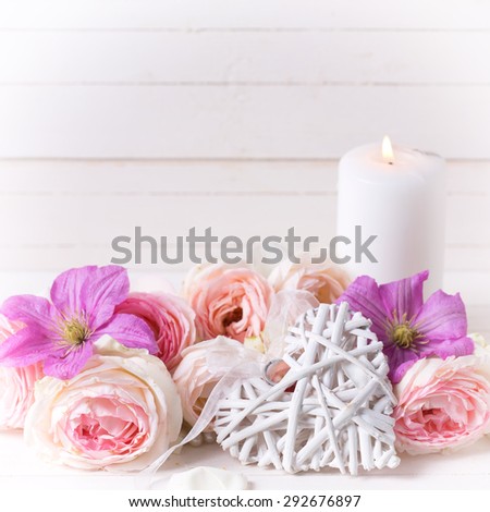 Decorative heart, pink roses  and violet clematis flowers and candles on white  wooden background.  Selective focus. Place for text. Square image.