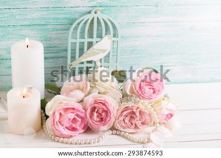 Background with  pink roses flowers and candles in ray of light  on white painted wooden background against turquoise wall. Selective focus.