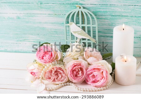 Background with  pink roses flowers and candles  on white painted wooden background against turquoise wall. Selective focus.