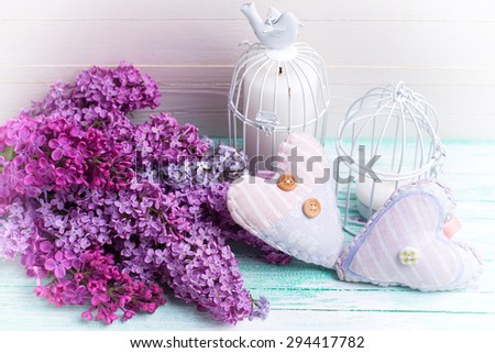 Background  with fresh lilac flowers, decorative hearts and candles in decorative bird cages  on turquoise painted wooden planks against white wall. Selective focus. Toned image.