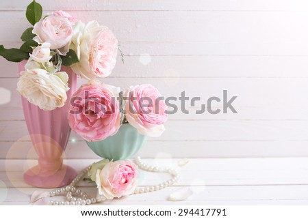 Sweet pink roses flowers in vases in ray of light  on white painted wooden background against white  wall. Selective focus. Place for text.