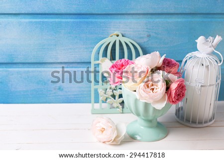 Pastel roses in turquoise vase and candle on white wooden  background against blue wall. Place for text. Selective focus.