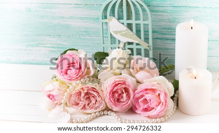 Background with  pink roses flowers and candles  on white painted wooden background against turquoise wall. Selective focus. Toned image.