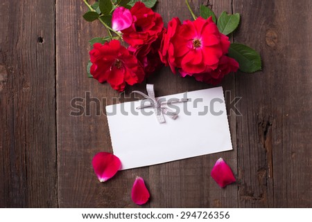 Empty tag and fresh red roses  on aged wooden background. Selective focus id on tag. Place for text.