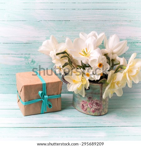 Background with colorful narcissus flowers and box with present  on turquoise painted wooden planks. Selective focus.  Square image.