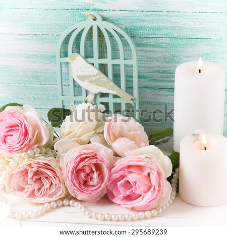 Background with  pink roses flowers and candles  on white painted wooden background against turquoise wall. Selective focus. Square image.