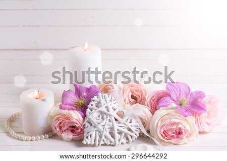 Decorative heart, pink roses  and violet clematis flowers and candles in ray of light on white  wooden background.  Selective focus. Place for text.