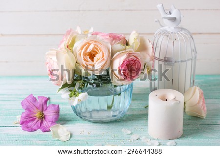 White roses, clematis and jasmine flowers  in vase and candles  on turquoise wooden background against white wall. Place for text. Selective focus.