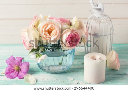 White roses, clematis and jasmine flowers  in vase and candles  on turquoise wooden background against white wall.  Selective focus. Toned image.