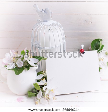 Postcard with tender apple blossom, candles in decorative bird cage and empty tag on white painted wooden planks. Selective focus. Place for text. Square image.