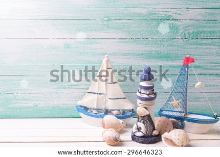 Decorative lighthouse,  sailing boats and marine items  in ray of light on wooden background. Sea objects on wooden planks. Selective focus. Place for text.