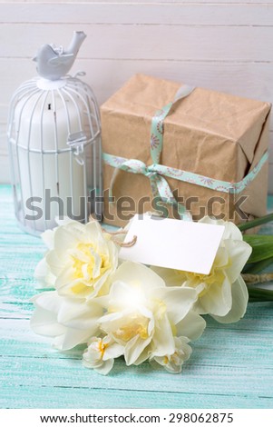 Postcard with fresh  daffodils flowers, candle and gift box  and tag on turquoise painted wooden planks against white wall. Selective focus is on flowers. Place for text.