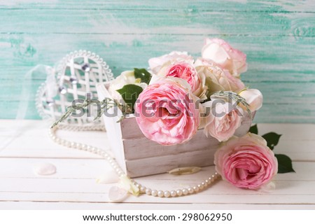 Background with sweet pink roses flowers  in wooden box on white painted wooden background against turquoise wall. Selective focus. Place for text.