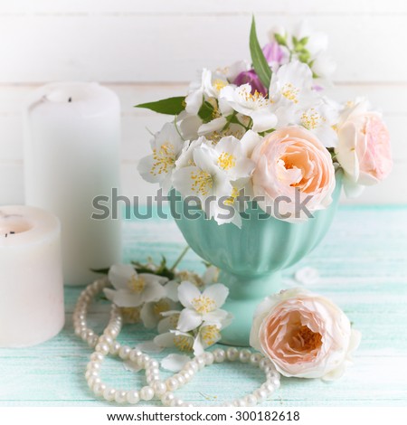 Pastel sweet roses and jasmine flowers  in vase, candles  on turquoise wooden background. Selective focus. Square image.