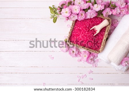 Spa or wellness setting. Pink sea salt in bowl with towels and pink flowers on white  wooden background. Selective focus is on salt.