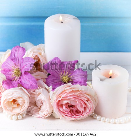 Fresh pink roses  and violet clematis flowers and candles on white  wooden background against blue wall.  Selective focus. Square image.