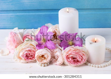 Fresh pink roses  and violet clematis flowers and candles on white  wooden background against blue wall.  Selective focus.