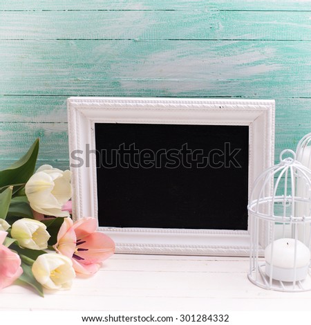 Fresh  spring white and pink tulips flowers, empty blackboard   and candles  on white  painted wooden planks against turquoise wall. Selective focus. Place for text. Square image.
