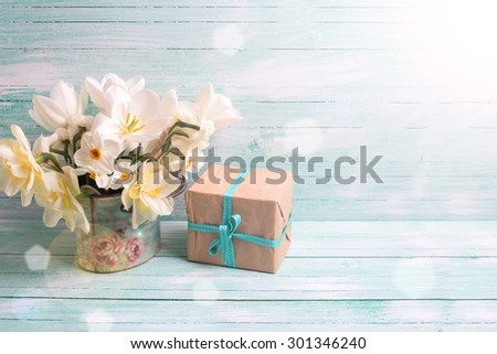 Background with colorful narcissus flowers and box with present  in ray of light  on turquoise painted wooden planks. Selective focus. Place for text.