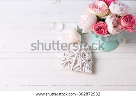 Pastel roses in turquoise vase and decorative heart on white wooden  background. Place for text. Selective focus.