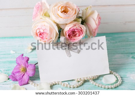 Pastel roses, clematis and jasmine flowers  in vase and empty tag on turquoise wooden background against white wall. Place for text. Selective focus.