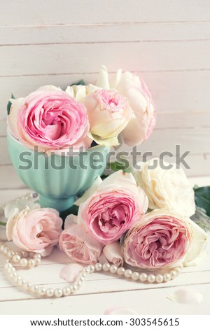 Sweet pink roses flowers in vase on white painted wooden background against white wall. Selective focus is on flower in vase. Toned image.