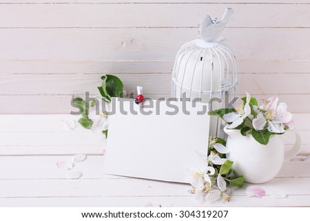 Postcard with tender apple blossom, candles in decorative bird cage and empty tag on white painted wooden planks. Selective focus. Place for text.