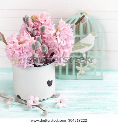 Background  with hyacinths,  willow flowers  in aged mug and decorative bird on turquoise painted wooden planks against white wall. Selective focus and empty place  for your text. Square image.