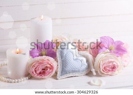 Decorative heart, pink roses  and violet clematis flowers , candles in ray of light  on white  wooden background.  Selective focus. Place for text.